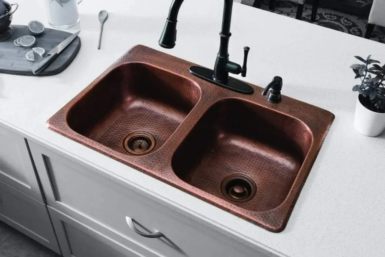 Fregadero doble de cobre martillado con grifo negro. Un truco para limpiar cobre con vinagre es ideal para mantenerlo brillante.