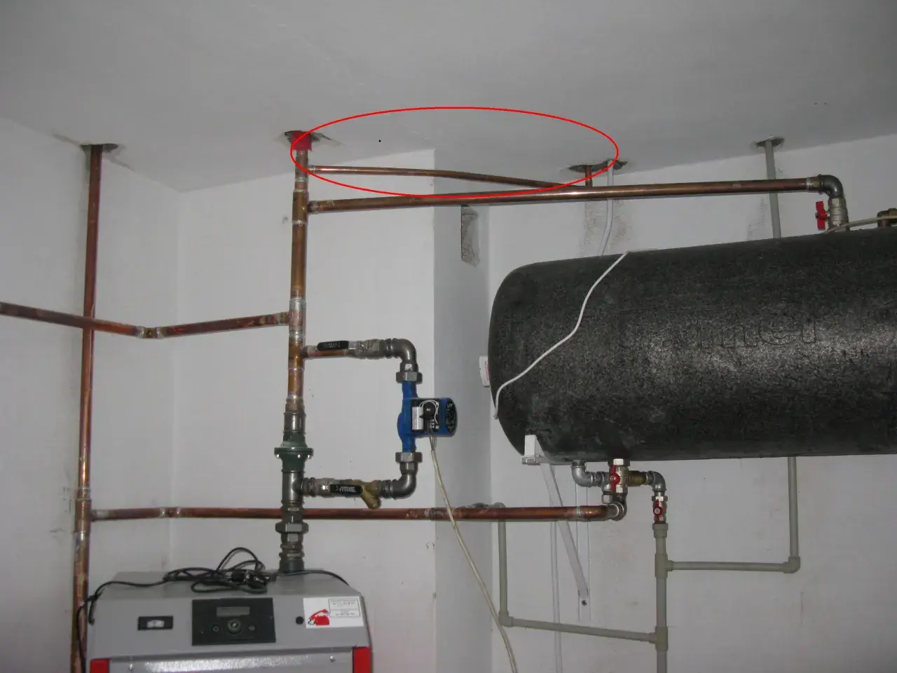 Instalacja hydrauliczna z bojlerem i pompą obiegową. Pokazano fragment instalacji, jak podłączyć zawór bezpieczeństwa do bojlera, z widocznymi rurami miedzianymi i złączkami.