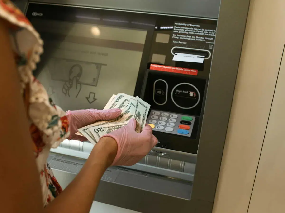 Une personne avec des gants roses prépare un dépôt d'argent liquide à un guichet automatique.