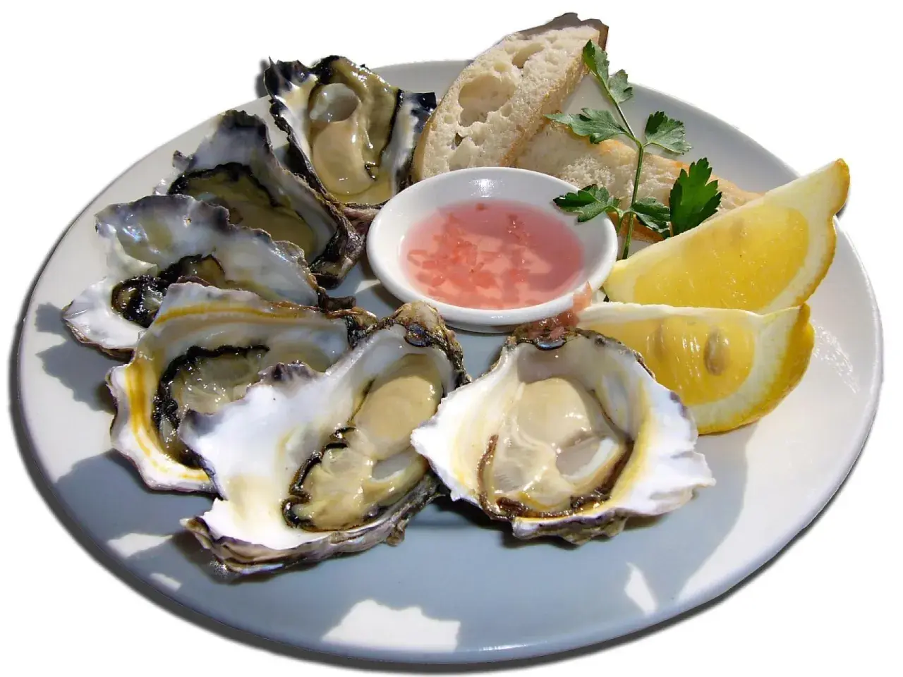 Ostra marisco fresco servida en plato con limón, pan y salsa rosada.
