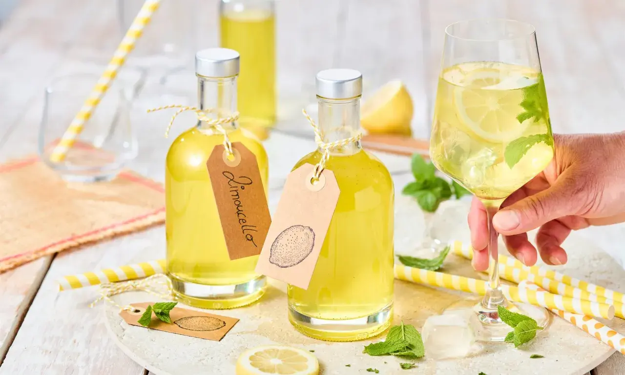 Zwei Flaschen mit gelbem Limoncello, ein Glas mit Eis, Zitrone und Minze. Das ist das original italienische Limoncello Rezept.
