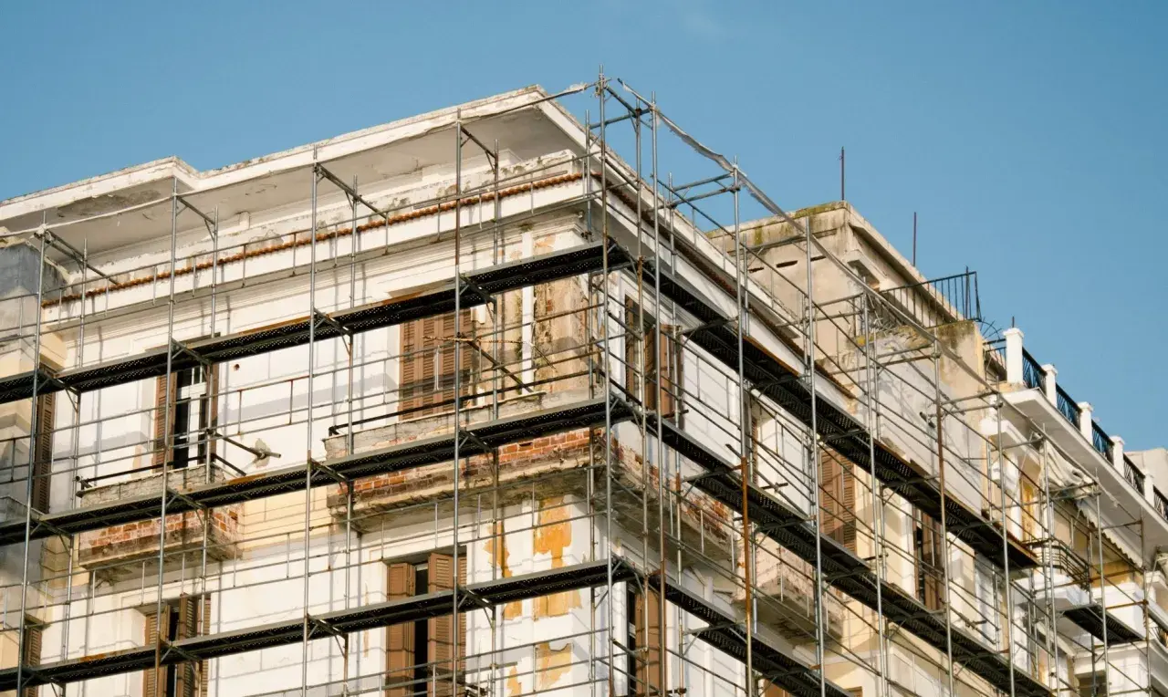 Bâtiment en rénovation, échafaudages pour aide ravalement façade sans isolation extérieur. Le ciel est bleu.