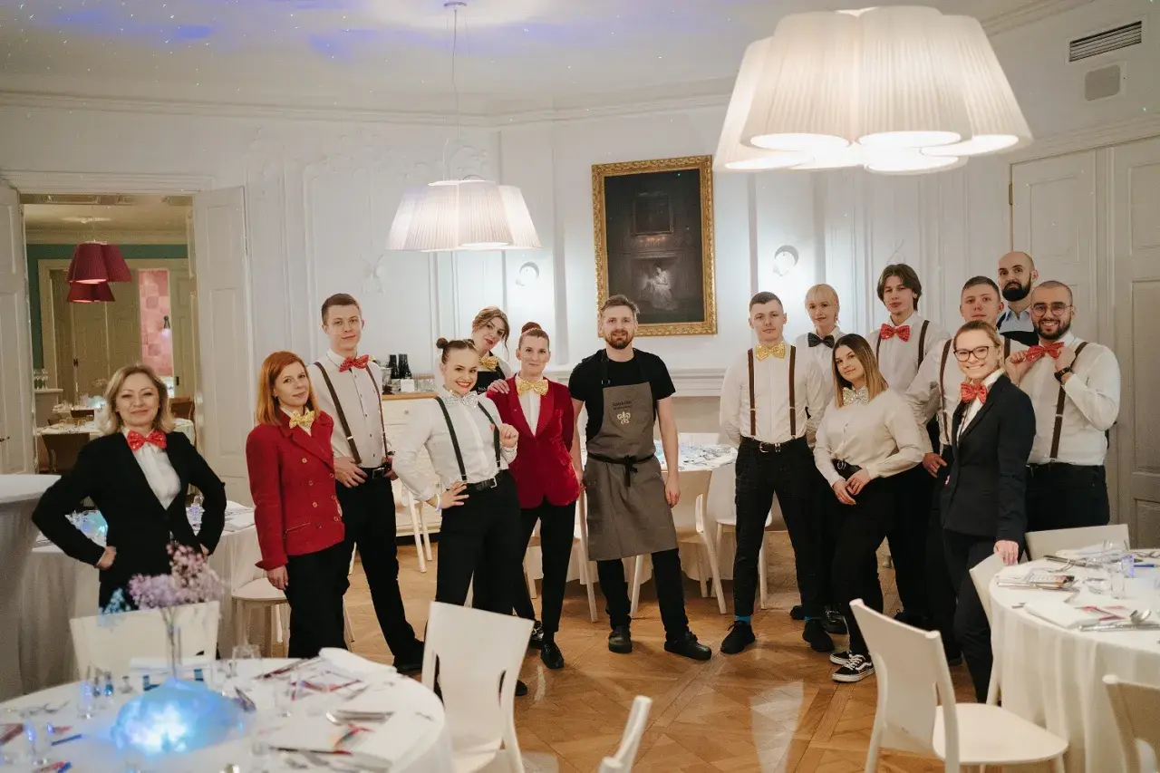 Zespół kelnerów w eleganckich strojach, z muszkami w stylu pellegrino, gotowy do obsługi przyjęcia.