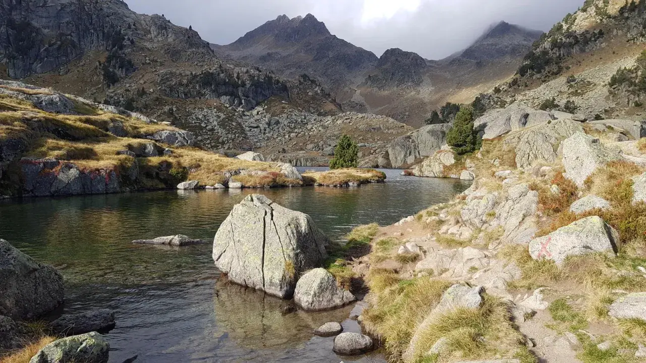 Paisaje sereno en el Vall d'Ora Gorgs, con un lago de aguas cristalinas rodeado de rocas y montañas escarpadas.