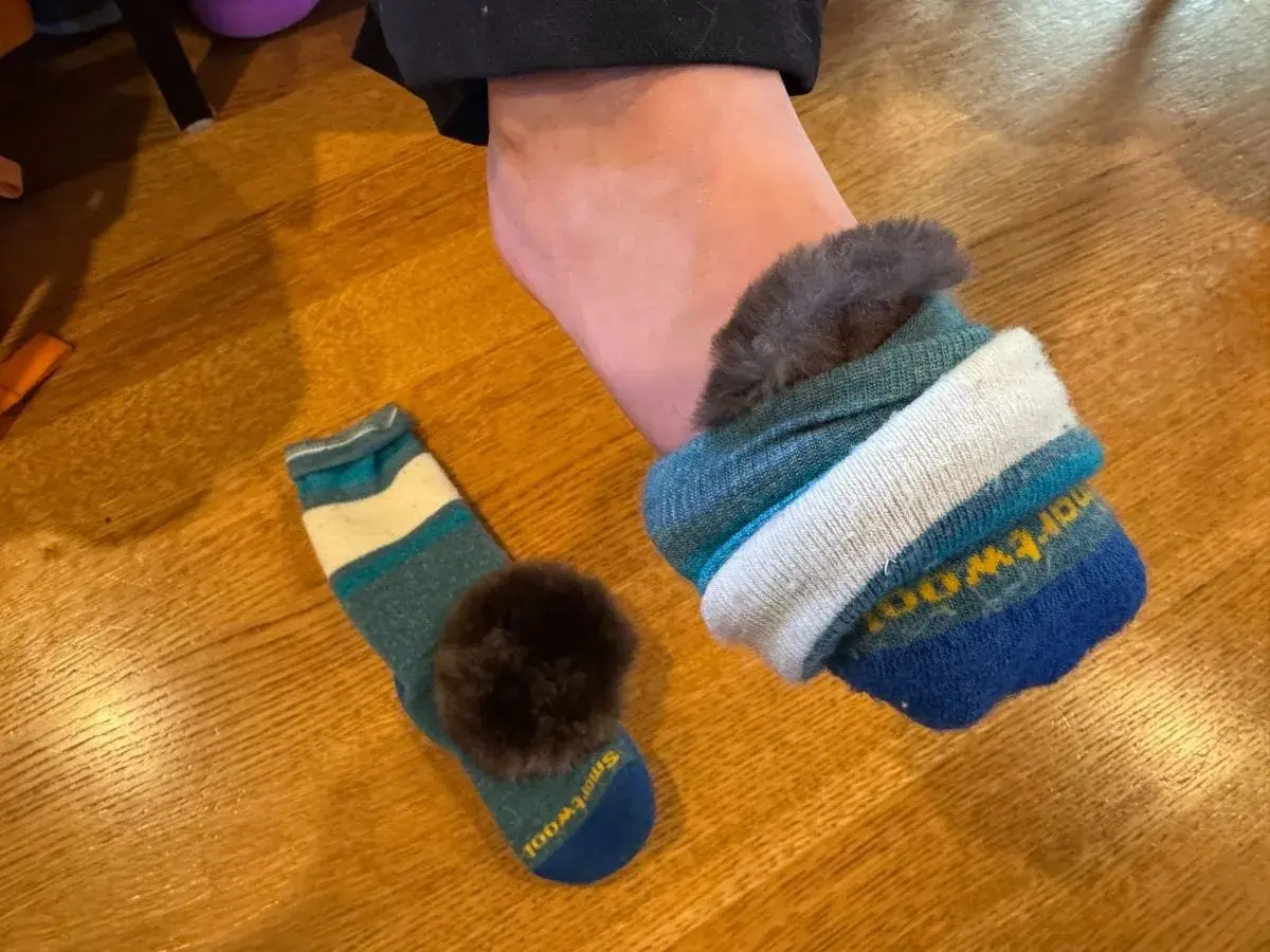 A foot wearing a fluffy-lined sock, with another striped sock and pom-pom nearby. Perfect for learning how to keep feet warm in boots.