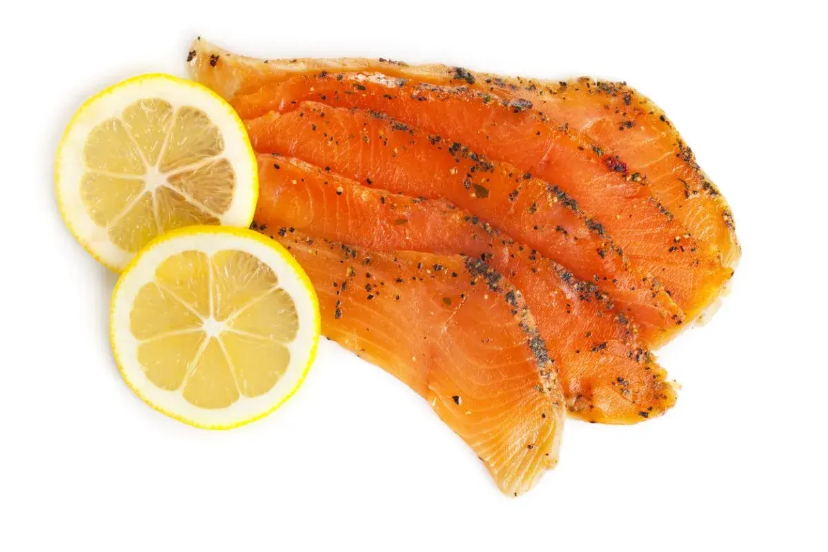 Skivor av gravad regnbåge med peppar och två citronskivor på vit bakgrund.