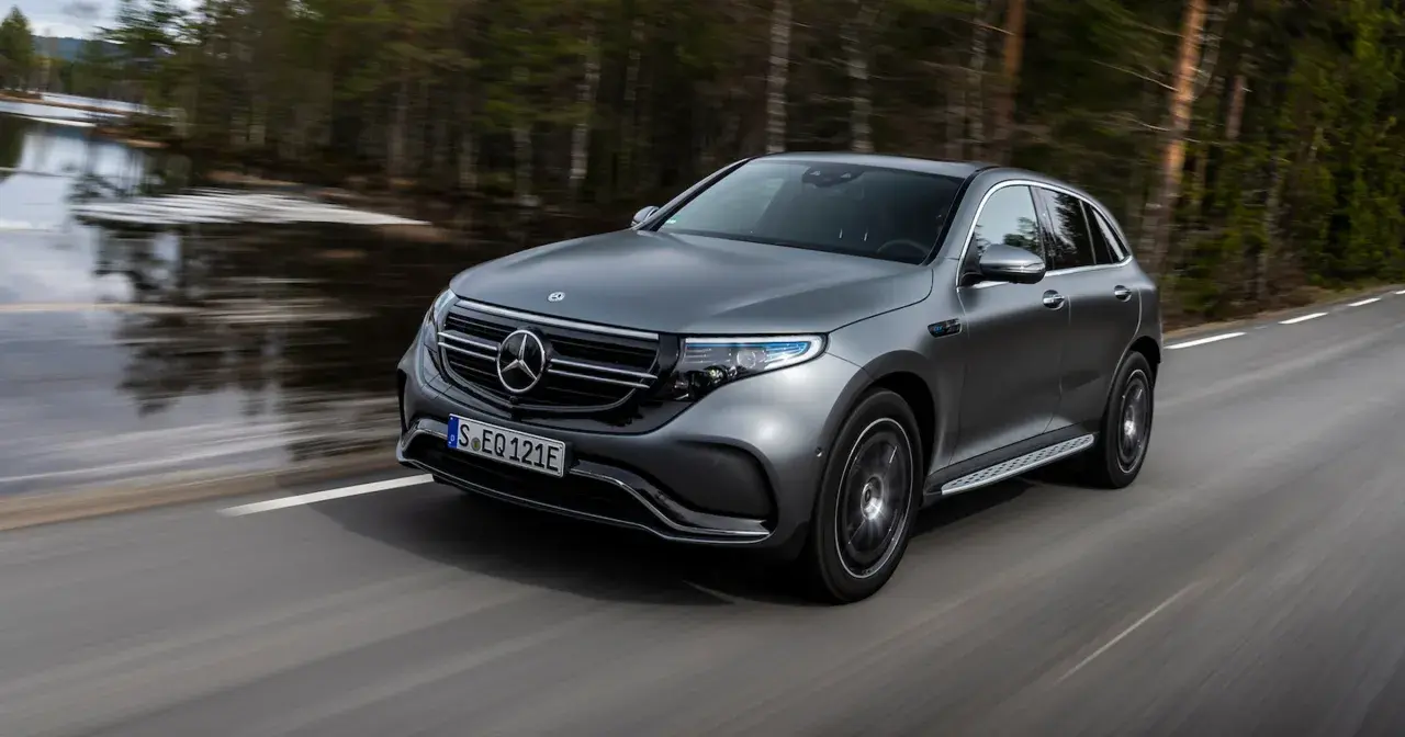 Szary Mercedes EQC jedzie po drodze wśród drzew.
