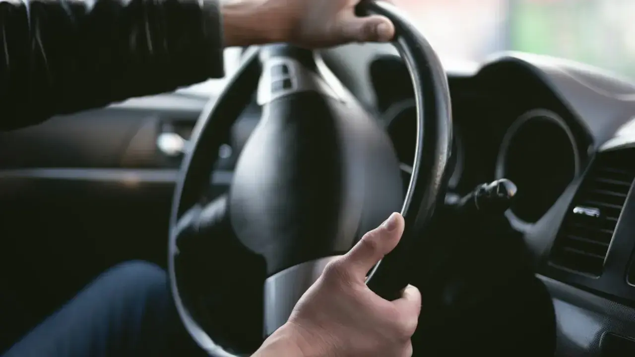 Manos sujetando el volante de un coche. La dirección del coche rota, indicando un giro o una maniobra.