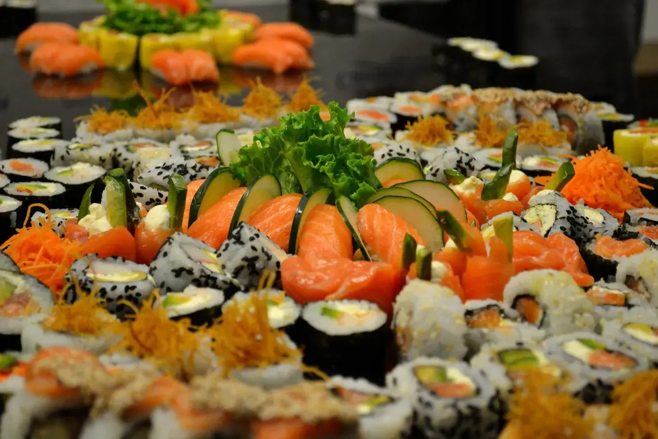 Mnóstwo sushi z łososiem, ogórkiem i sałatą. Wśród nich widać kawałki ryby maślanej, tworząc apetyczną kompozycję.