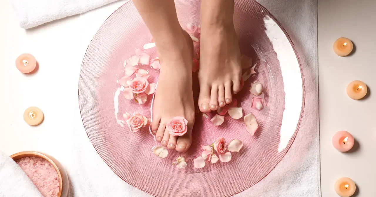 Relaks w domowym spa: stopy w różowej kąpieli z płatkami róż i świecami. To właśnie jest pedicure co to znaczy – dbanie o stopy.