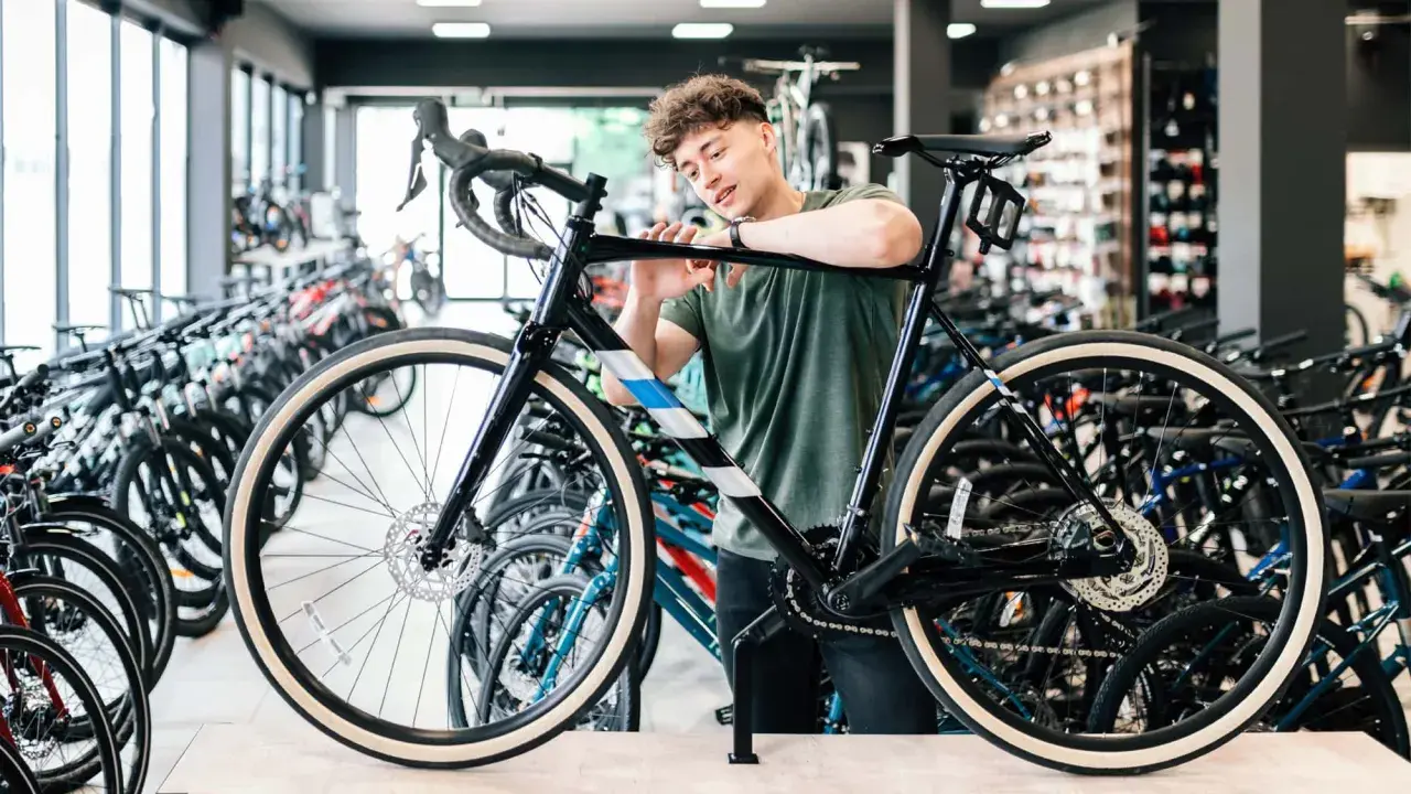 Ein junger Mann prüft ein schwarzes Fahrrad in einem Geschäft, um zu entscheiden, welches Fahrrad zu ihm passt. Viele Fahrräder stehen im Hintergrund.