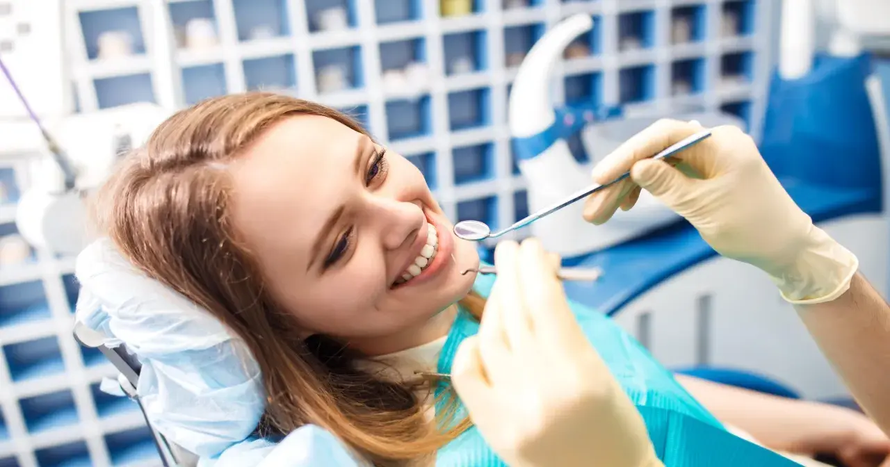 Uśmiechnięta kobieta u dentysty, badanie zębów lusterkiem i narzędziem.