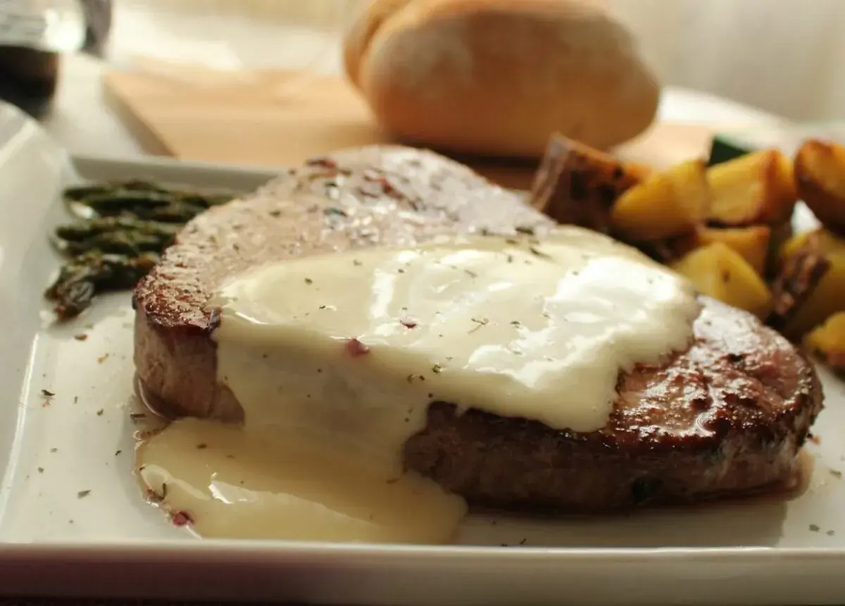 Filete redondo cubierto con una cremosa salsa blanca, acompañado de espárragos y patatas asadas.