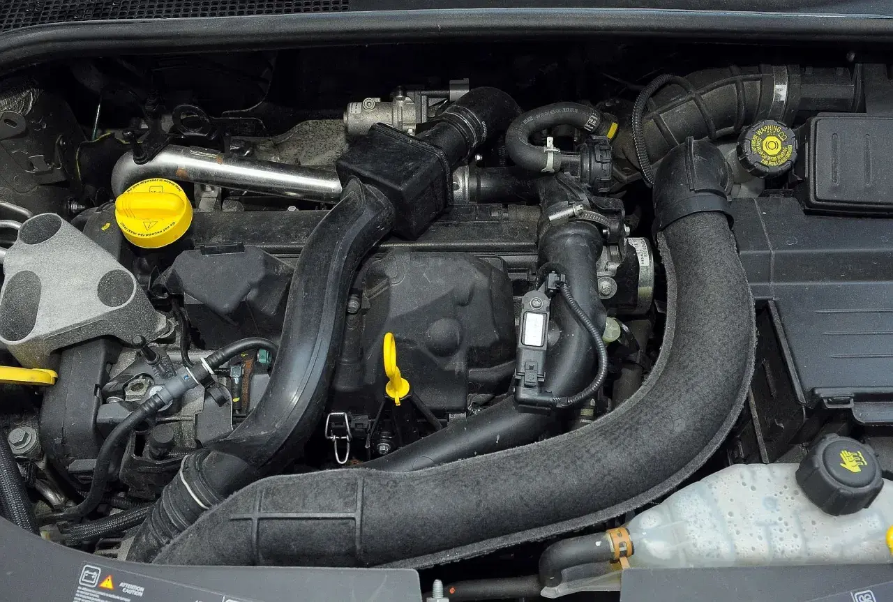Silnik Renault Clio 3 z widocznymi przewodami, czujnikami i żółtym korkiem oleju.