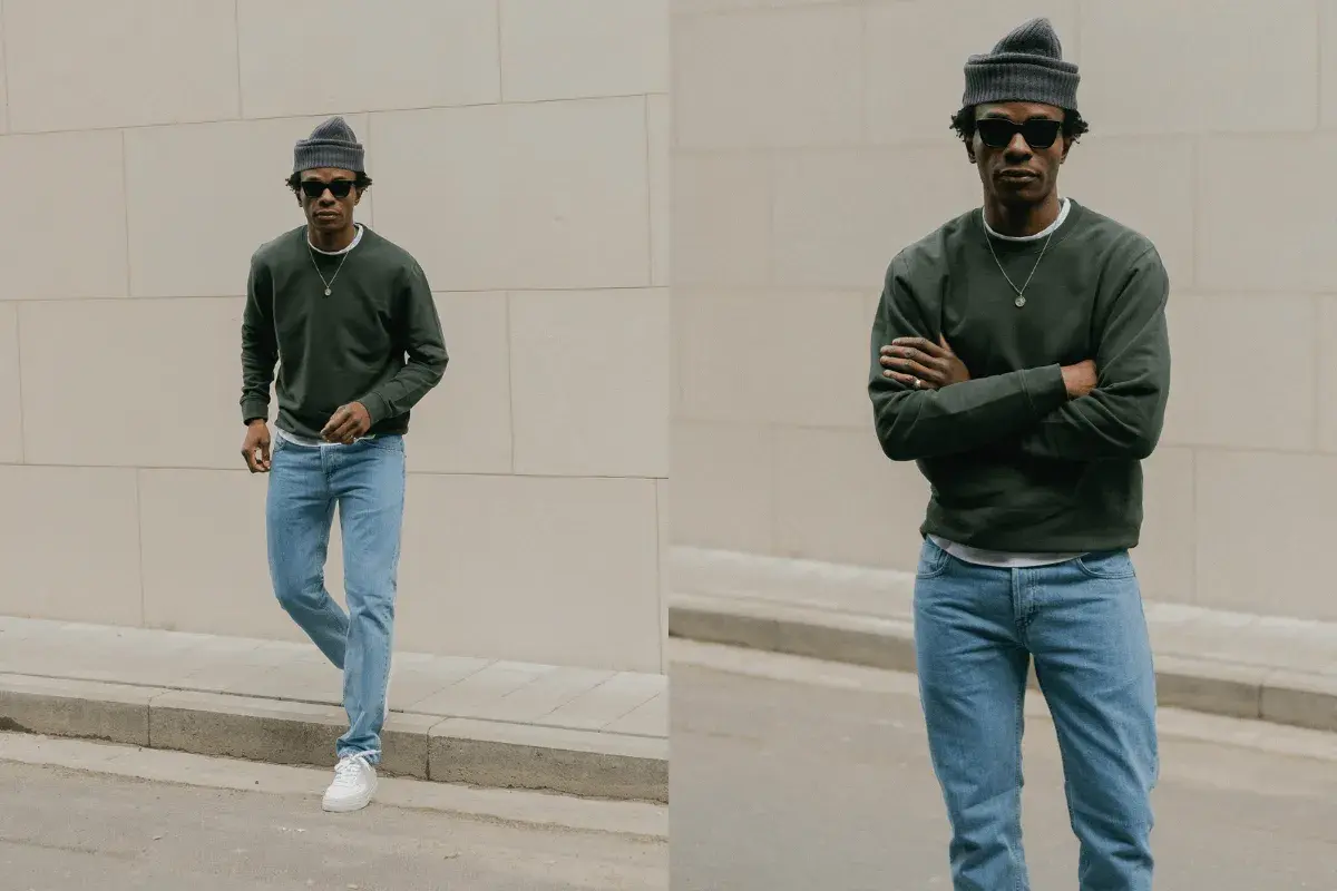 Un homme porte une tenue jean bleu décontractée, un pull vert foncé et un bonnet gris.