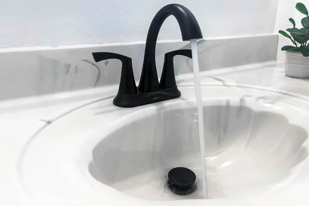 Rubinetto nero moderno in un lavandino bianco, con acqua che scorre. Uno stilema fad che aggiunge un tocco di eleganza.