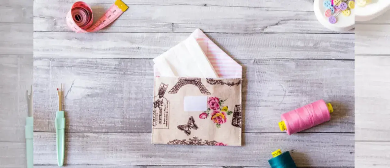 Sobres de tela con diseño de París y flores, junto a carretes de hilo, cinta métrica y descosedor.