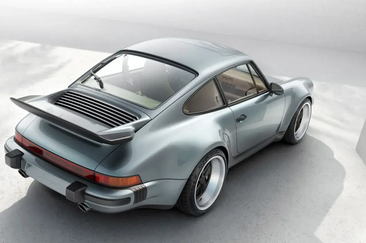 En ikonisk Porsche 80-tals coupé i ljusblått, med sin karaktäristiska bakvinge och breda fälgar.