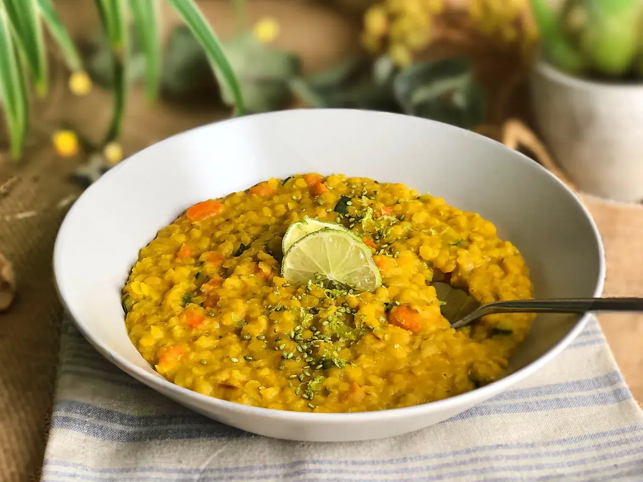 Un tazón de lentejas al curry con zanahoria y calabacín, decorado con rodajas de lima y ralladura.