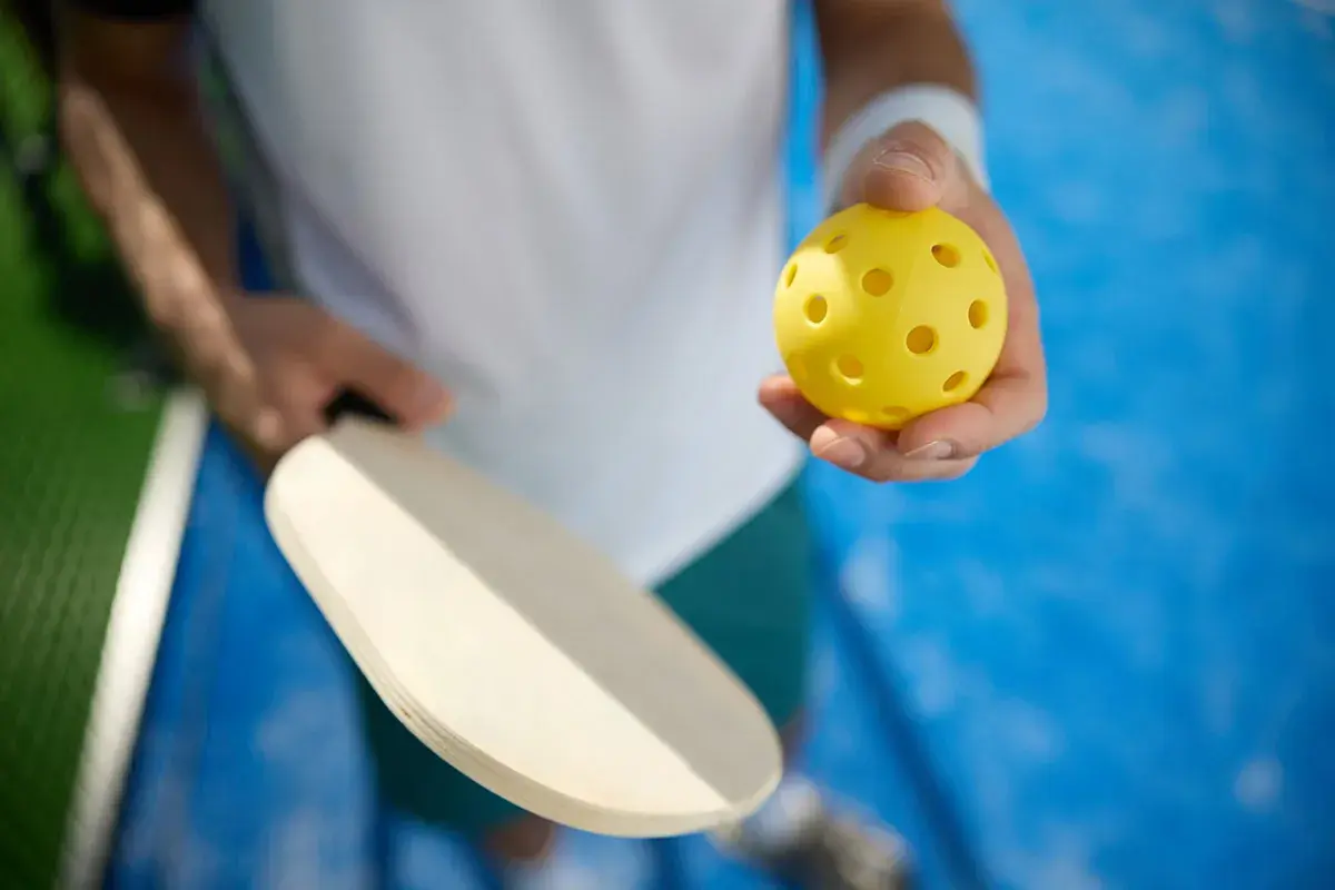 Gracz trzyma rakietkę i żółtą piłeczkę. Idealny sprzęt do treningu mobility i gry w pickleball.