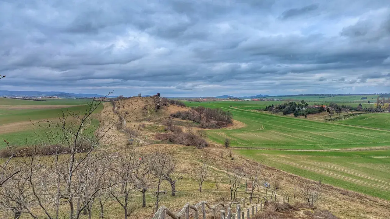 Blick ins Bodetal: Wanderweg führt durch hügelige Landschaft mit grünen Feldern und kahlen Bäumen unter dramatischem Himmel.