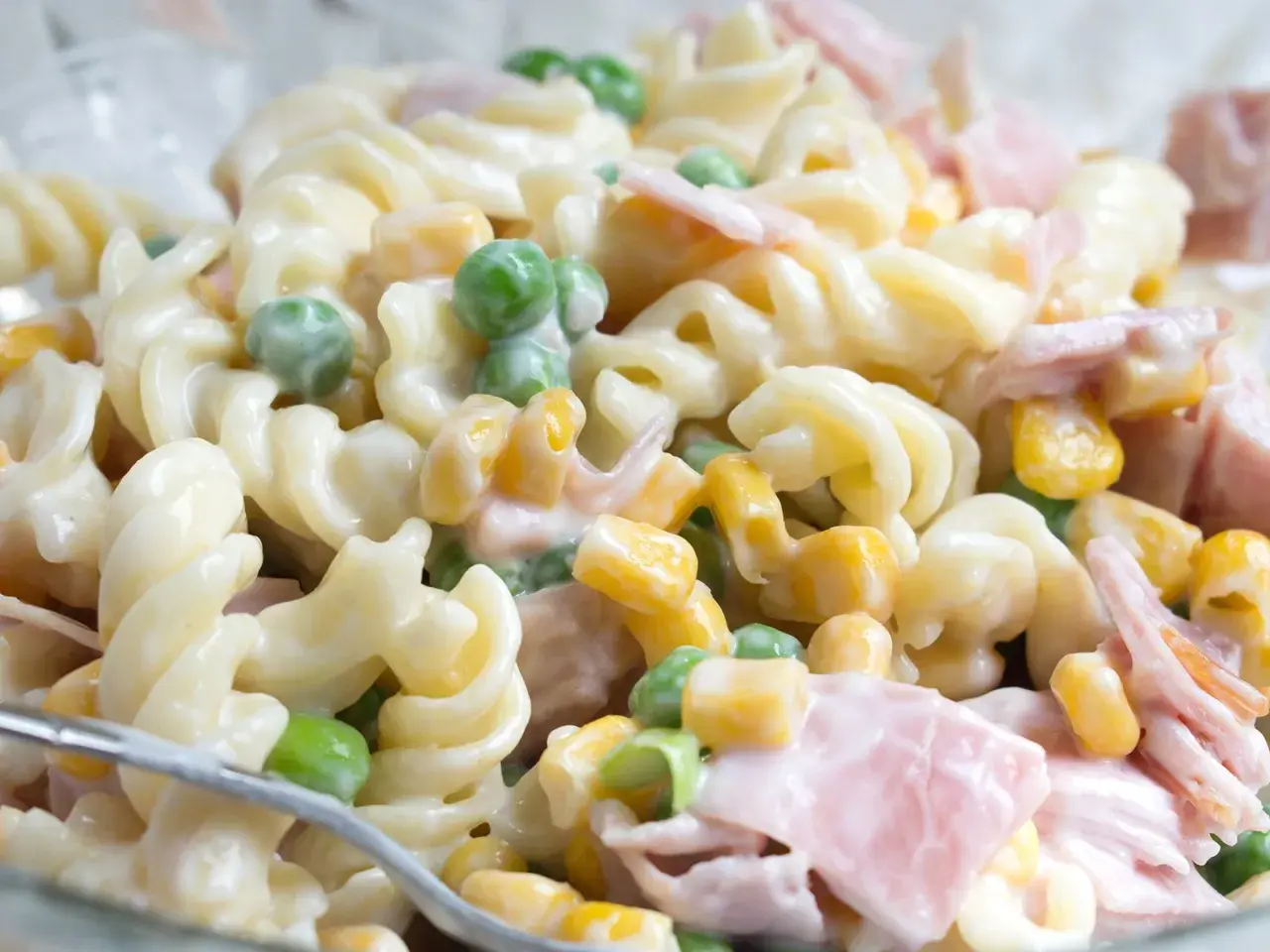 Ein einfacher Nudelsalat mit Spiralnudeln, Erbsen, Mais und Schinken in cremiger Soße.