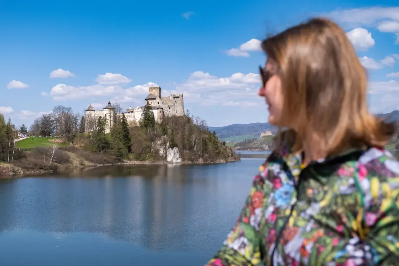 Widok na zamek nad jeziorem, z kobietą w kolorowej kurtce na pierwszym planie. To wspaniałe niedzica atrakcje turystyczne.