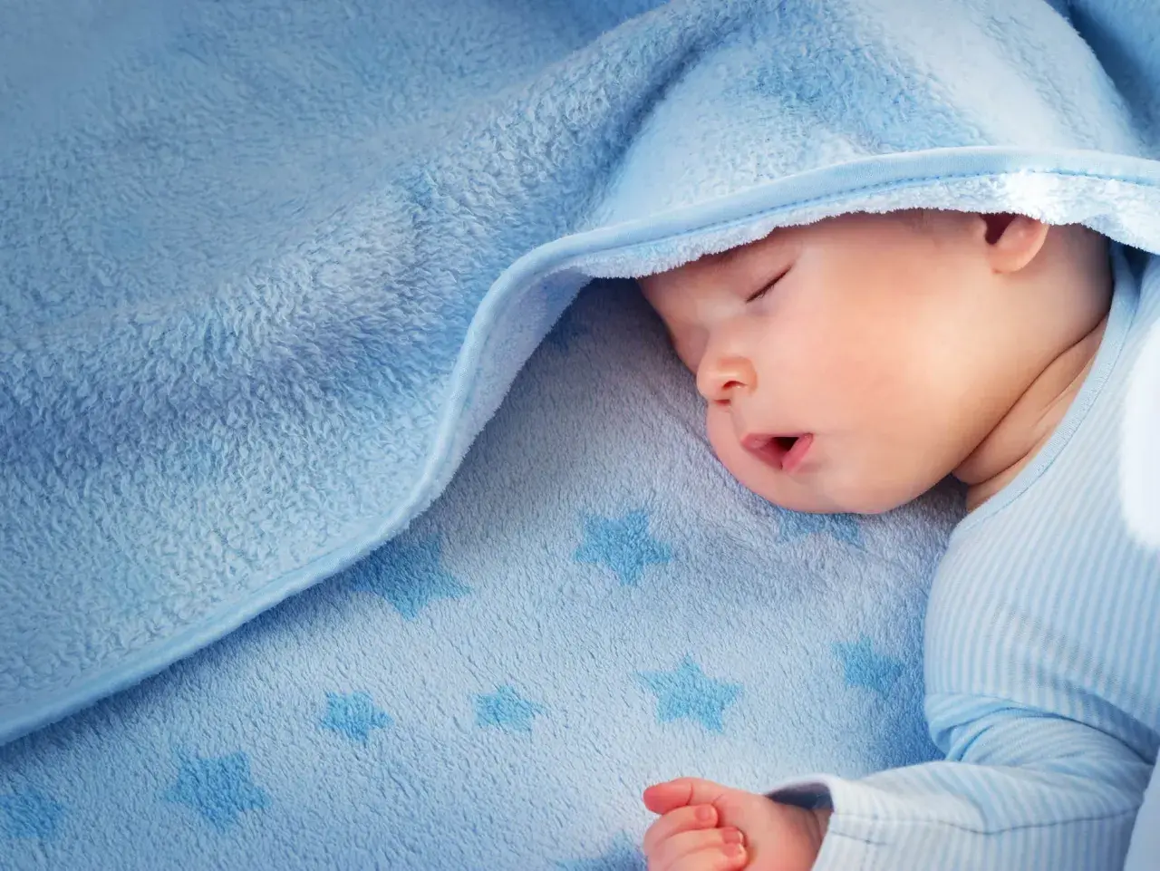 Sover gott under ett mjukt, blått täcke med stjärnor. Liten bebis svettas lite i sömnen.
