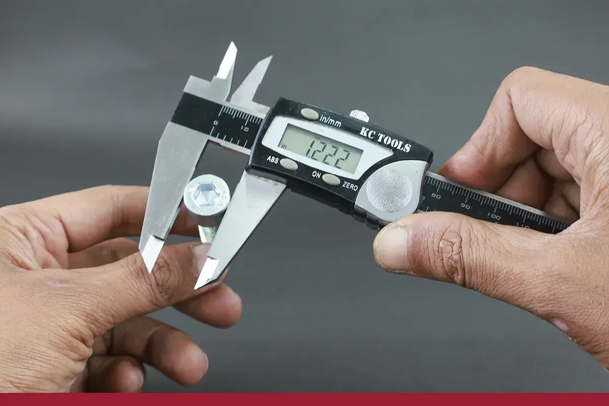 Manos sujetan un tornillo hexagonal y un calibre digital para su calibre medicion. La pantalla muestra 1.222.