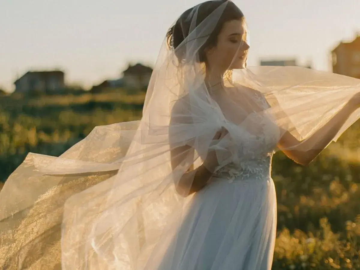 Novia con velo ondeando al atardecer, como si soñara con vestido de novia en un campo.
