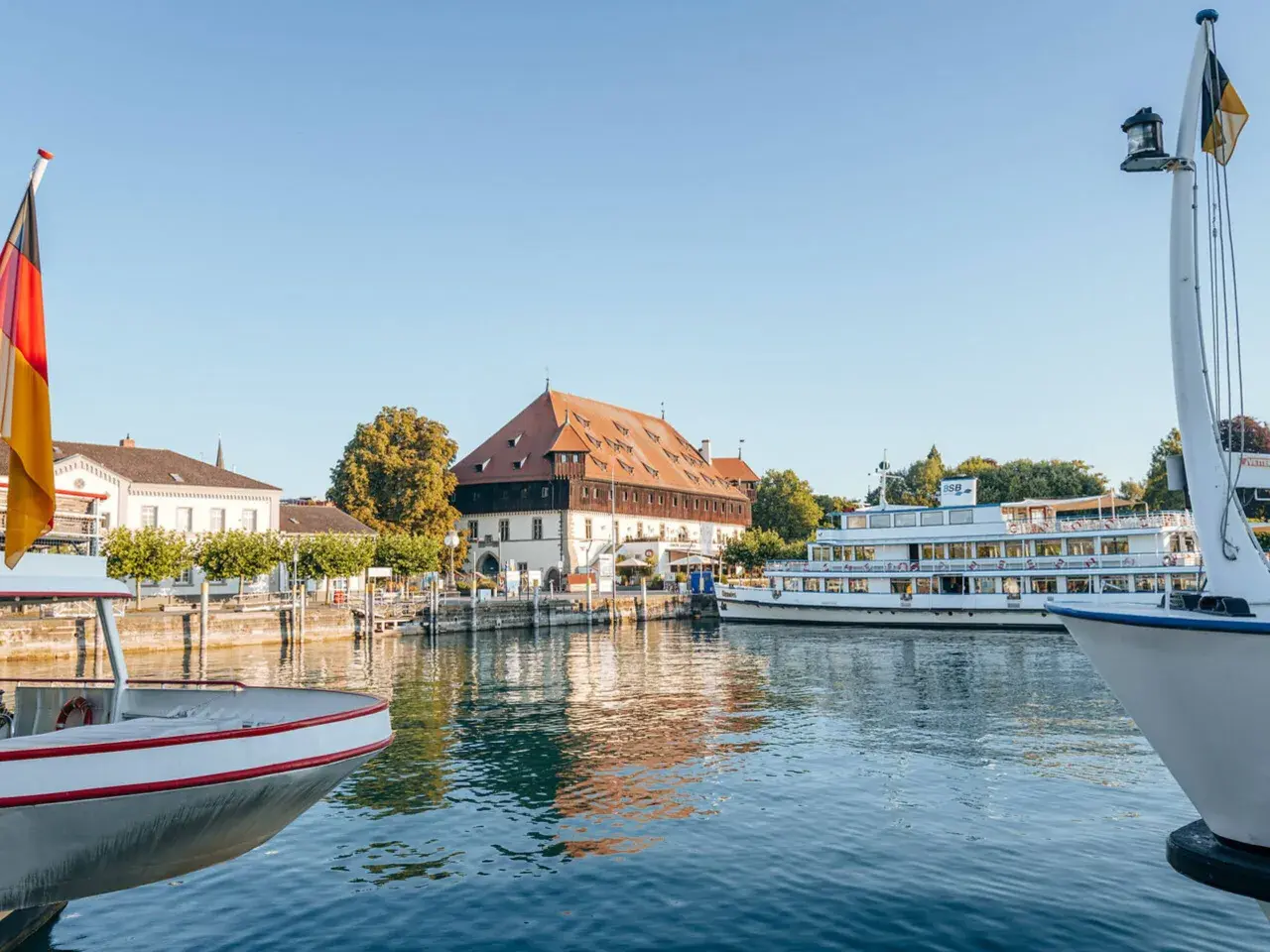 Boote am Bodensee, deutsche Flagge weht. Ein historisches Gebäude und ein Ausflugsschiff laden zu Konstanz Events ein.
