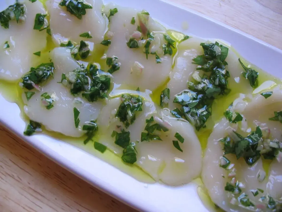 Délicieux carpaccio de saint jacques crues, nappé d'une vinaigrette aux herbes fraîches et à l'ail. Un plat léger et savoureux.