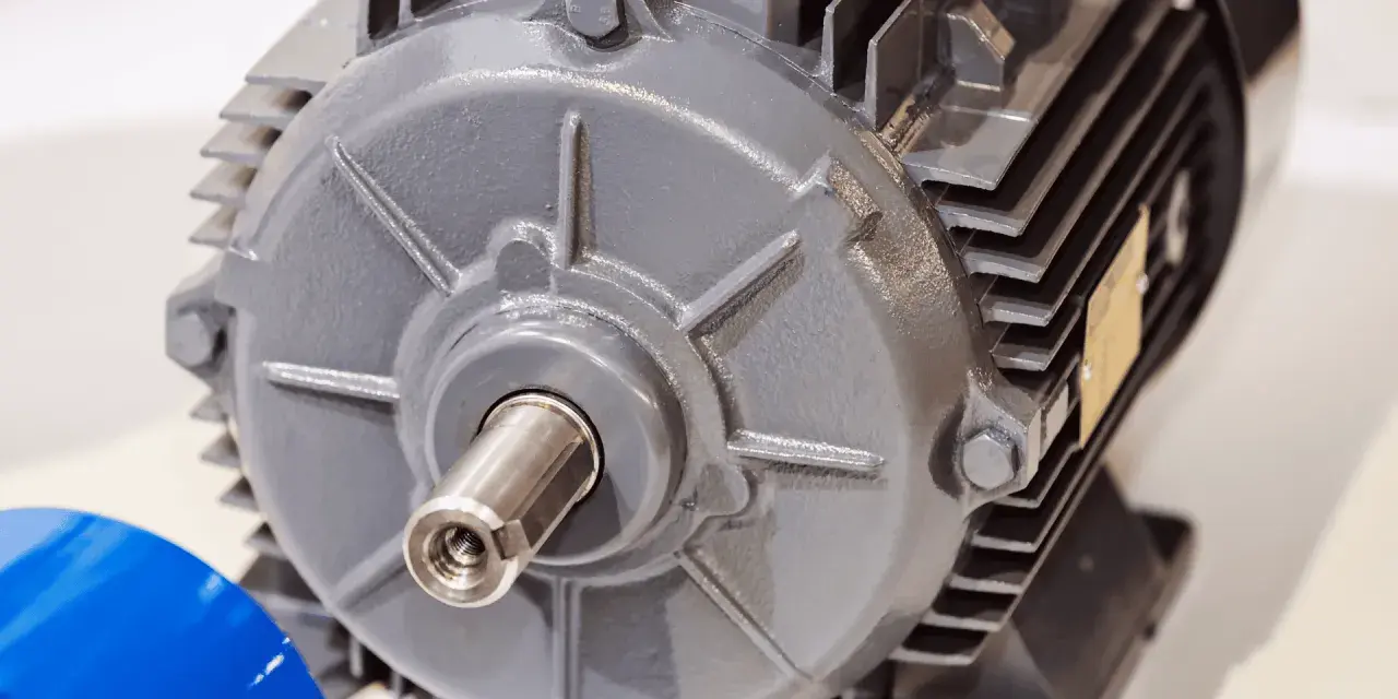 Dettaglio di un motore elettrico grigio, con albero motore visibile e una targhetta dorata.