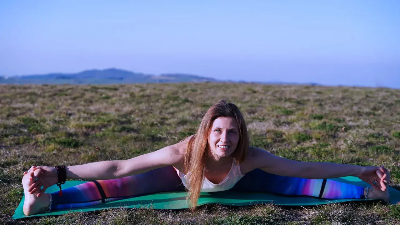 Donna in posa yoga all'aperto, con le gambe divaricate, che lavora sul primo chakra sessualità.