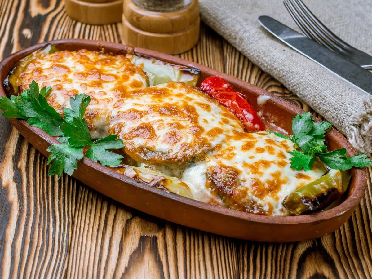 Kotlet po góralsku zapieczony z serem i warzywami w glinianym naczyniu, udekorowany natką pietruszki.