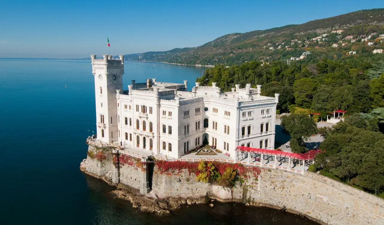Vitt slott vid havet i Trieste, Italien, med en italiensk flagga på tornet.