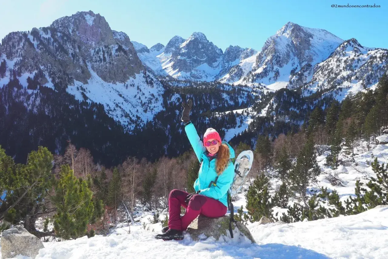 Mujer con raquetas de nieve saluda en un paisaje nevado de **Pallars Sobirà**. Montañas imponentes y bosques cubiertos de nieve crean un telón de fondo espectacular.