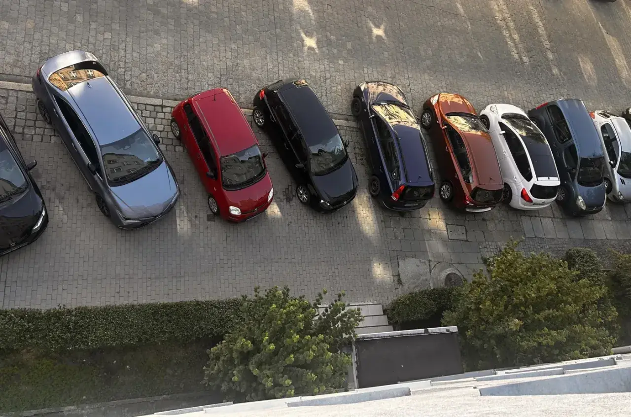 Szary samochód, czerwony, czarny, granatowy, rudy, biały, ciemnogranatowy i srebrny stoją na parkingu. Może to być inspiracja do wypełnienia wniosku o miejsce parkingowe wzór.