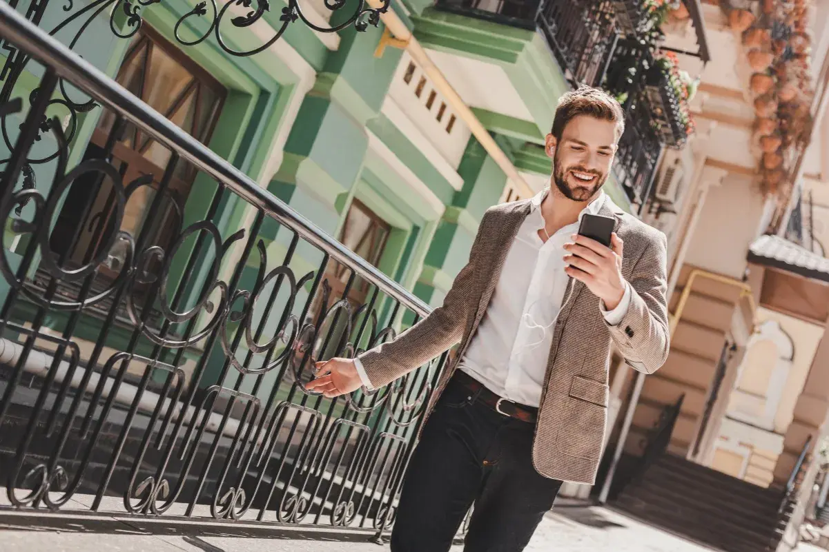 Ein Mann im casual chic Outfit mit Sakko und Jeans lächelt, während er auf sein Smartphone schaut.