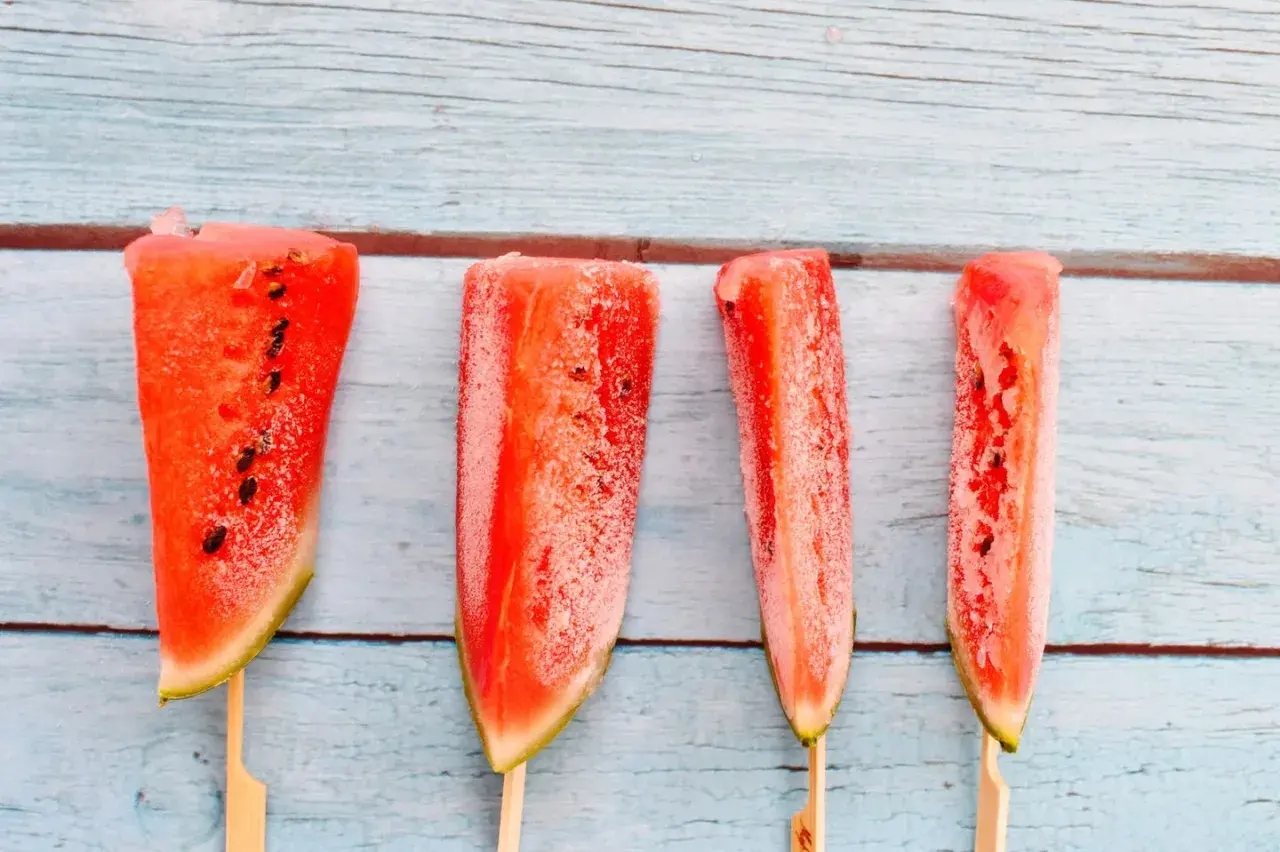 Vier Wassermelonenstücke auf Stäbchen, bereit zum Wassermelone einfrieren. Perfekt für heiße Sommertage.