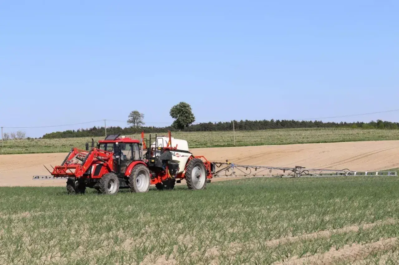 Czerwony traktor z opryskiwaczem polowym pracuje na polu. Tabela mieszania oprysków pomaga rolnikowi w precyzyjnym zabiegu.