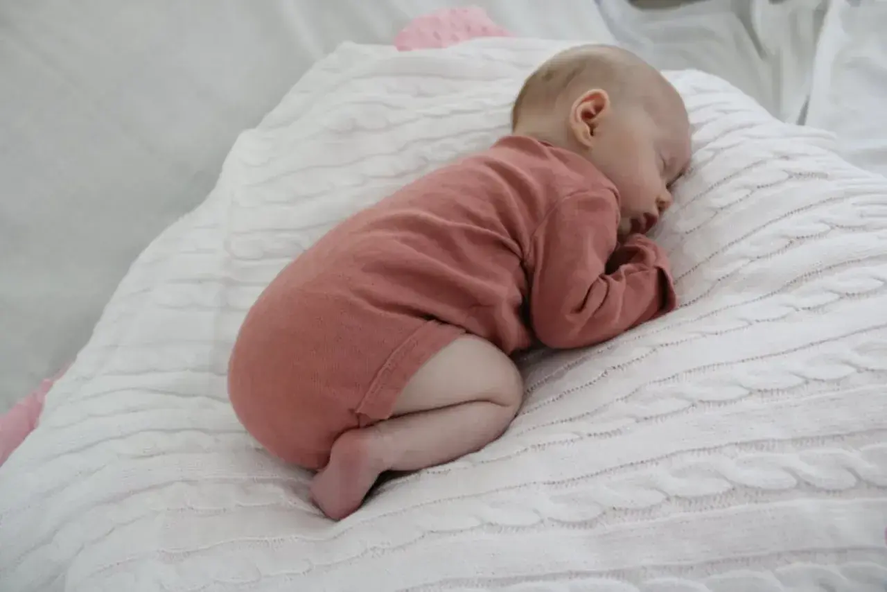 Sover sött på en vit stickad filt, en liten bebis i en rosa body. Hoppas bebisen inte hosta.