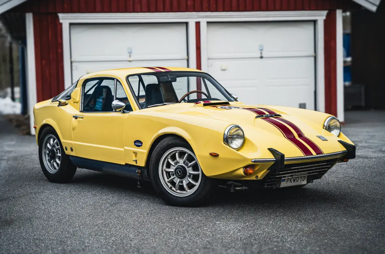 Gul Saab Sonett 2 med röda ränder, parkerad framför ett rött garage.