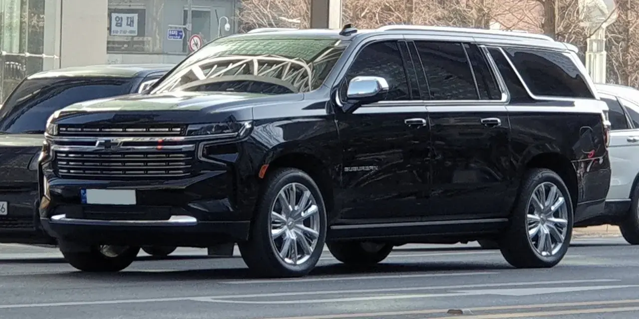 Czarny Chevrolet Suburban, który wygląda jak największe auto na świecie, z chromowanymi felgami i błyszczącą atrapą chłodnicy.