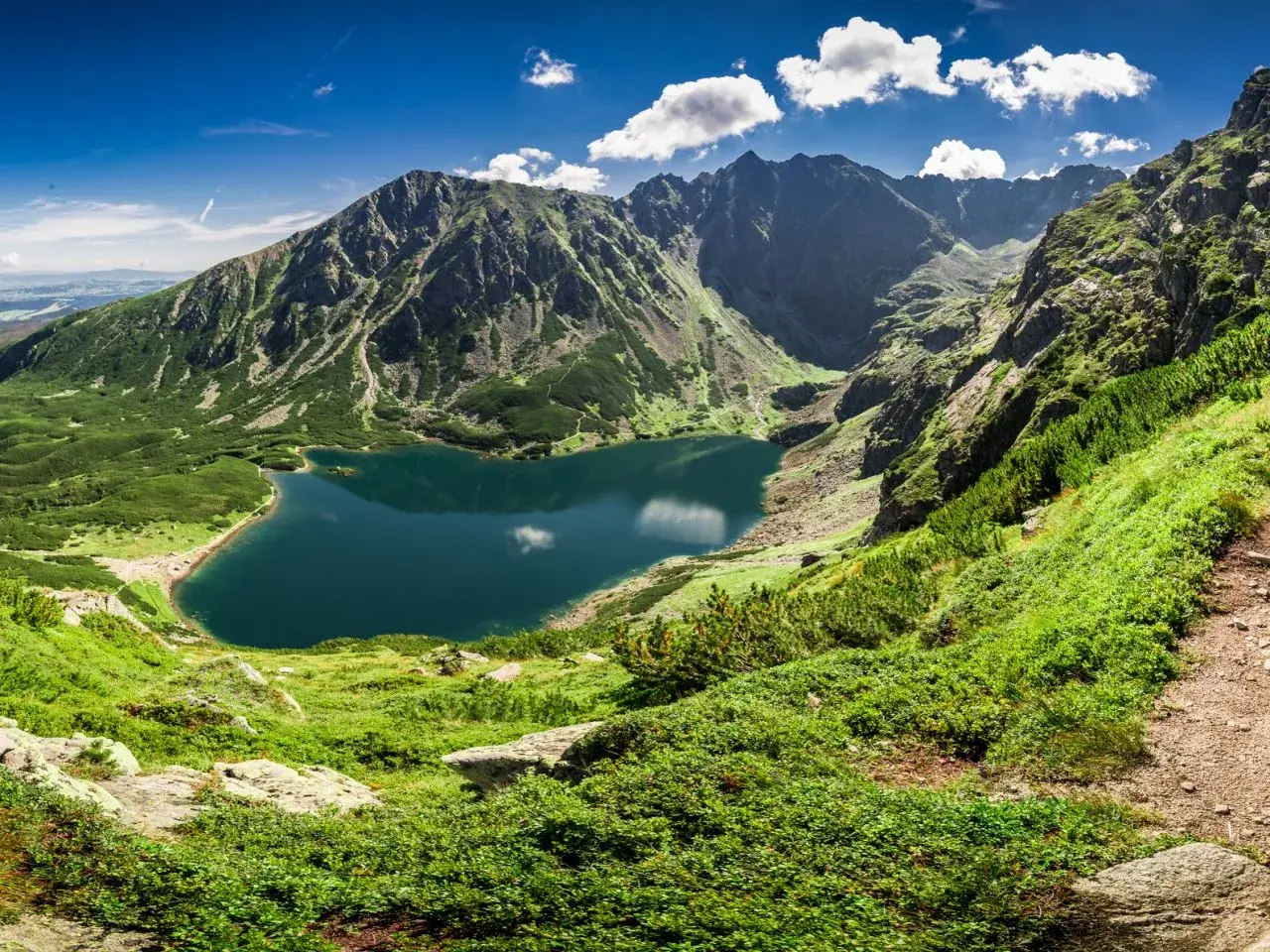 Bergsee in Polen, umgeben von grünen Hängen und schroffen Gipfeln. Die beste Reisezeit für solche Ausblicke ist der Sommer.