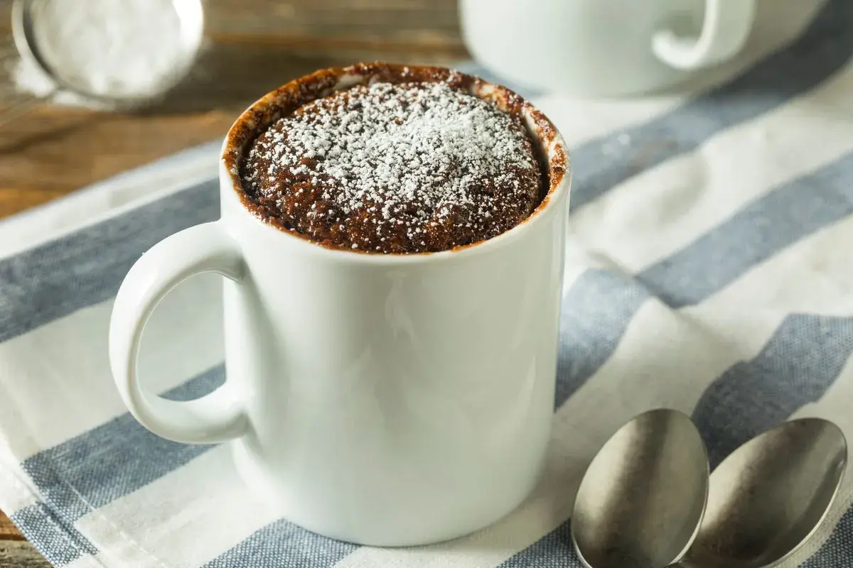 Un delizioso mug cake al cioccolato, spolverato di zucchero a velo, pronto per essere gustato.