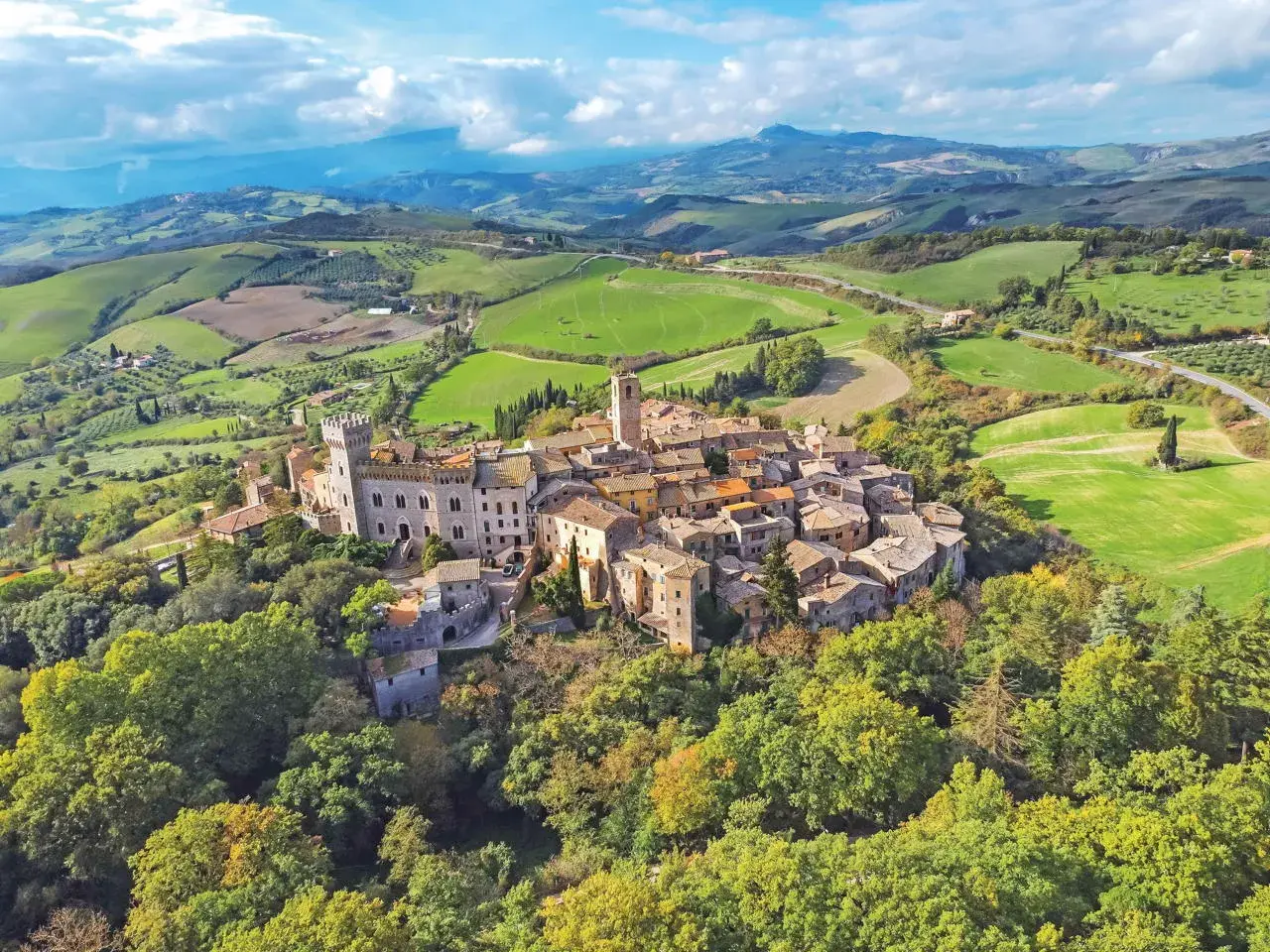 Un borgo toscano arroccato su una collina, circondato da dolci colline verdi e campi coltivati. Un esempio dei borghi toscani più belli.