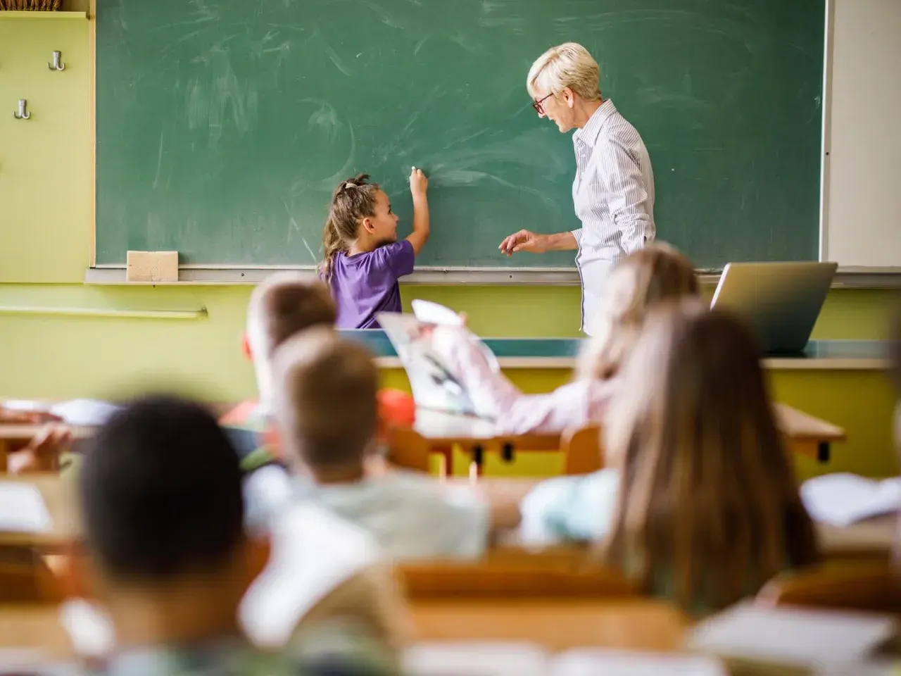Eine Lehrerin steht vor einer Tafel, während ein Kind schreibt. Es ist schön, Lehrer zu sein und Wissen zu vermitteln.