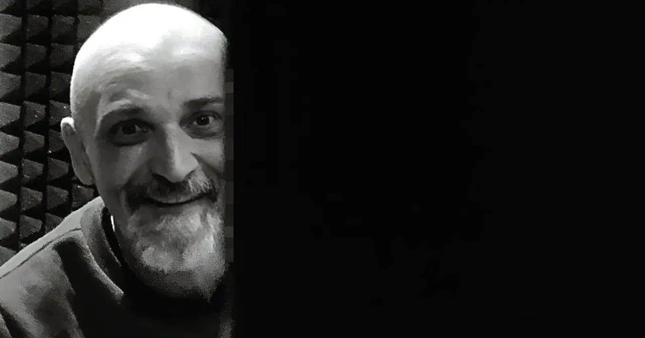 Uśmiechnięty Wojciech Sęp Dudziński, z charakterystyczną brodą i łysą głową, w studiu nagraniowym.