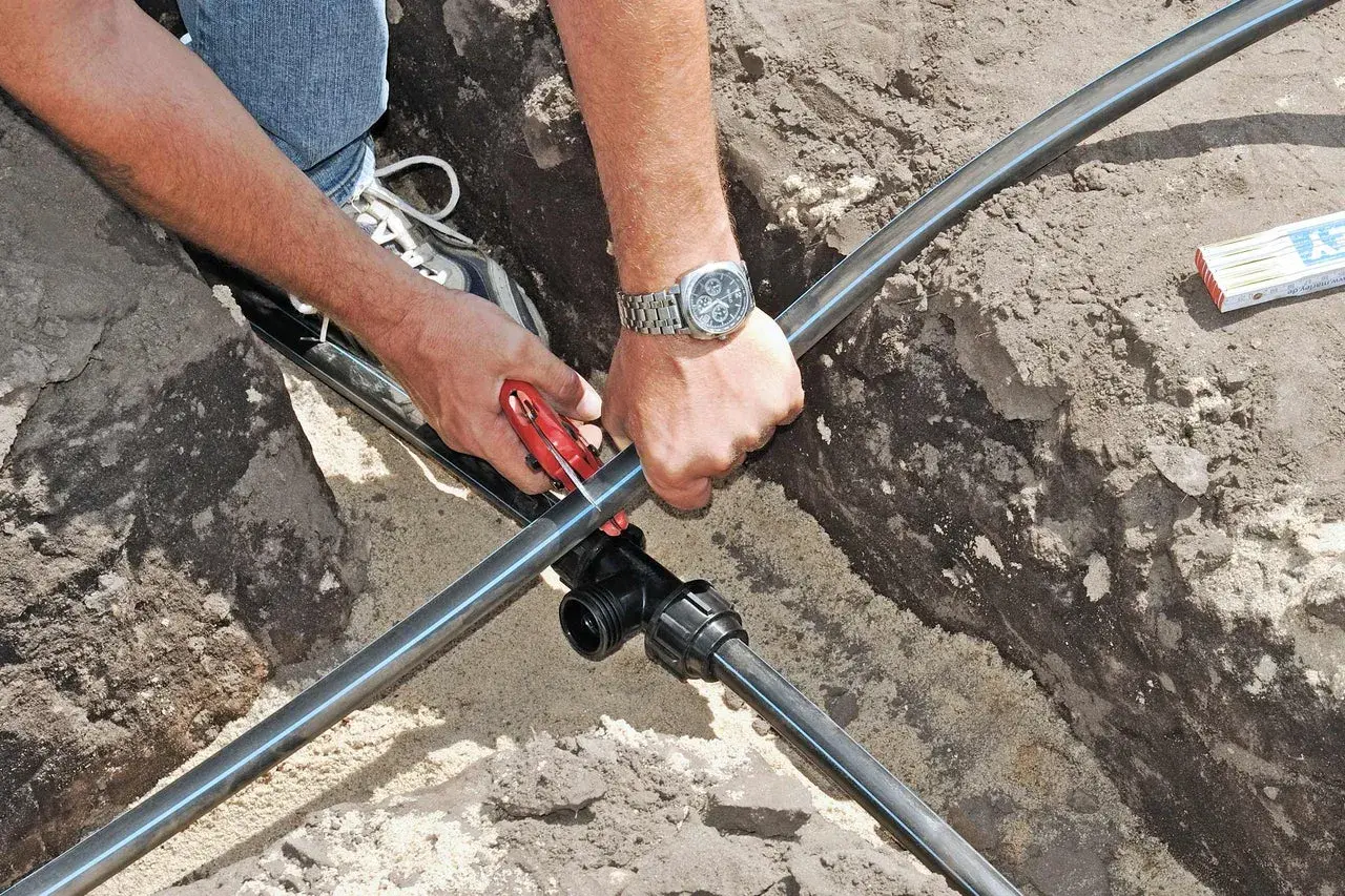 Hände schneiden Kunststoffrohr für die wasserleitung verlegen. Ein T-Stück wird vorbereitet.
